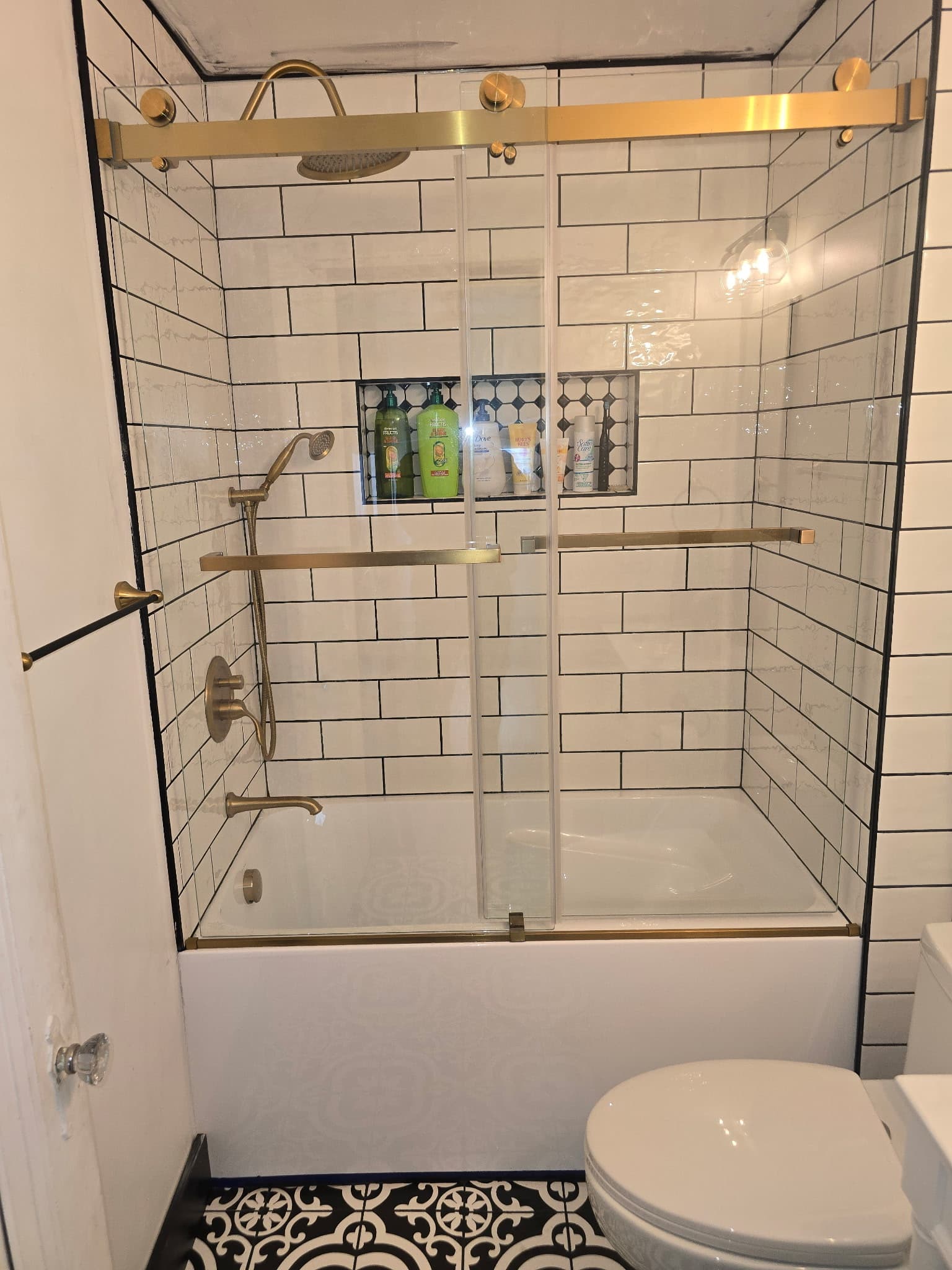 Subway tile shower with brass-framed sliding glass door and rainfall shower head