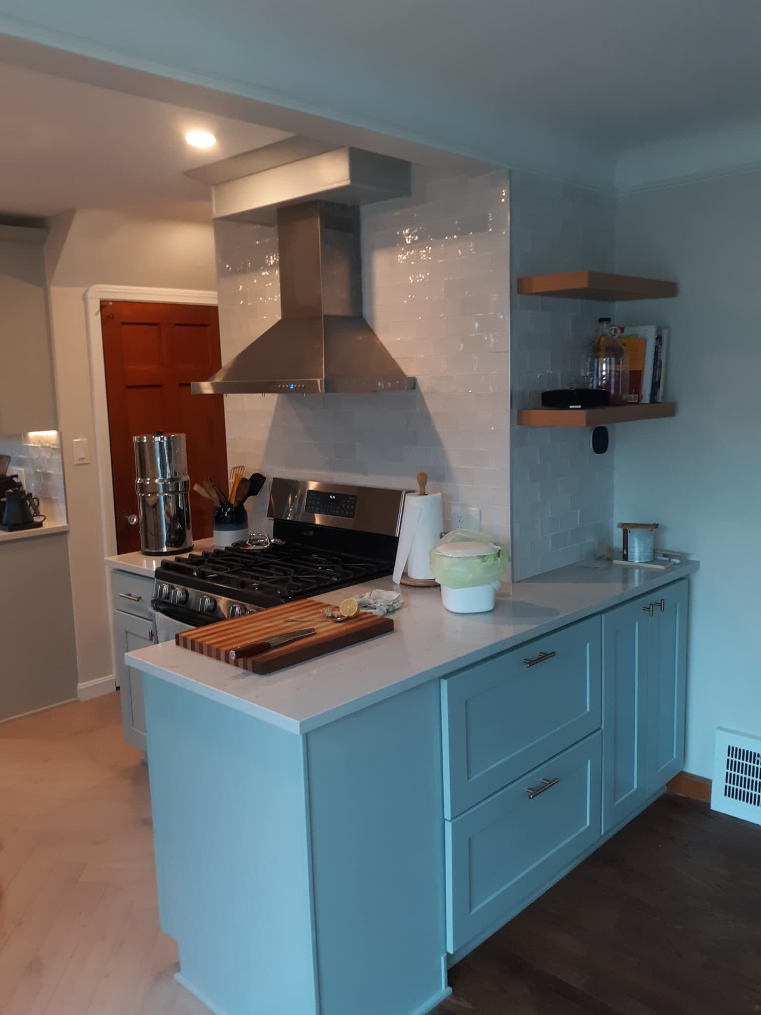 Teal shaker kitchen with stainless gas range, hood, and white subway tile backsplash