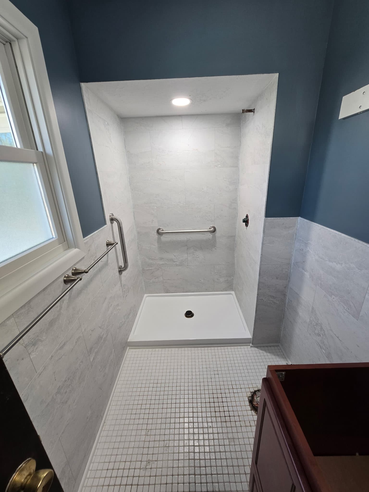 ADA-friendly walk-in shower with grab bars, white tile floor, and marble-look walls