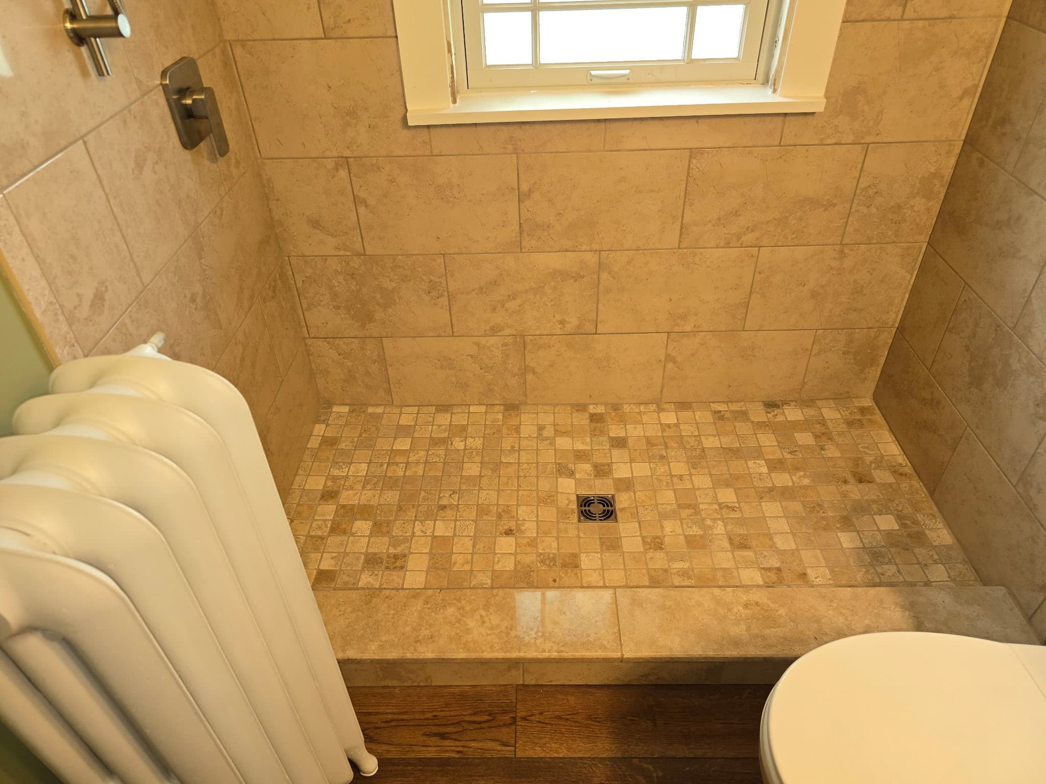 Travertine mosaic shower floor under a window