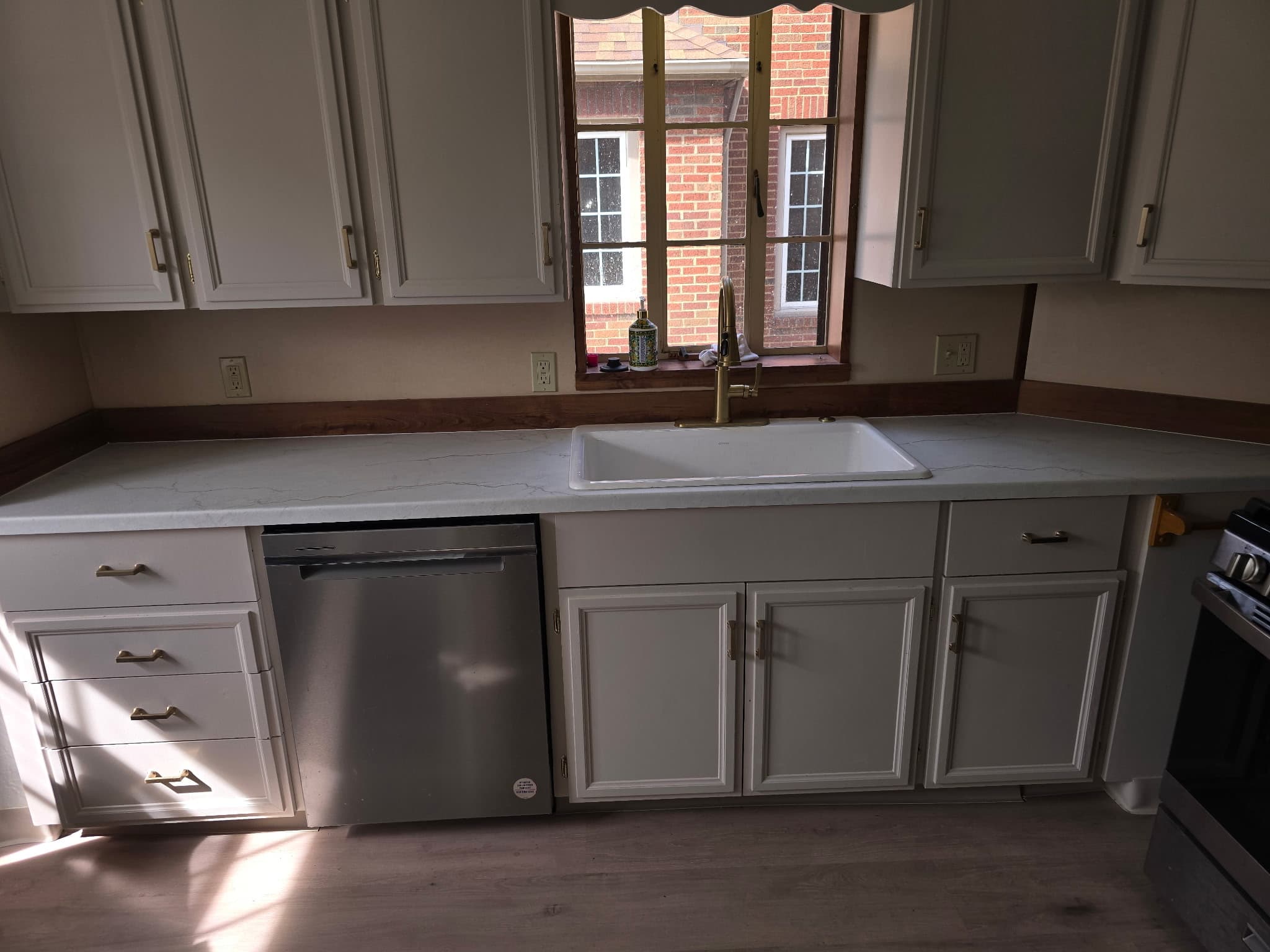 Light gray kitchen with brass hardware, white quartz, and farmhouse sink