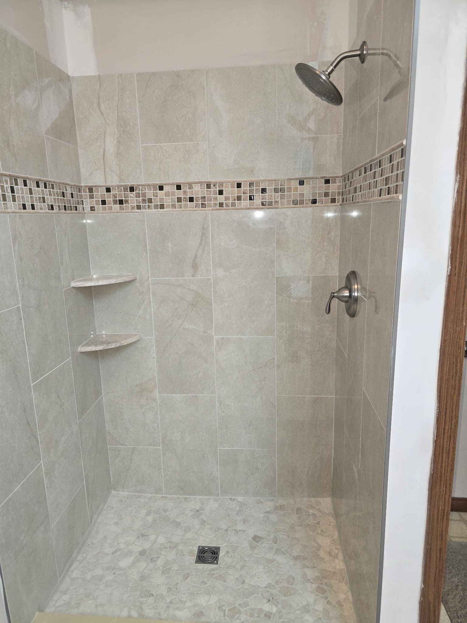 Tiled walk-in shower with glass mosaic accent stripe and river-rock pebble floor