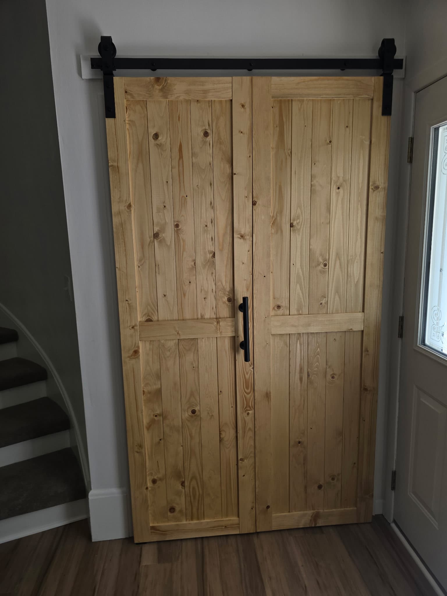 Custom natural pine sliding barn doors with black hardware in entryway
