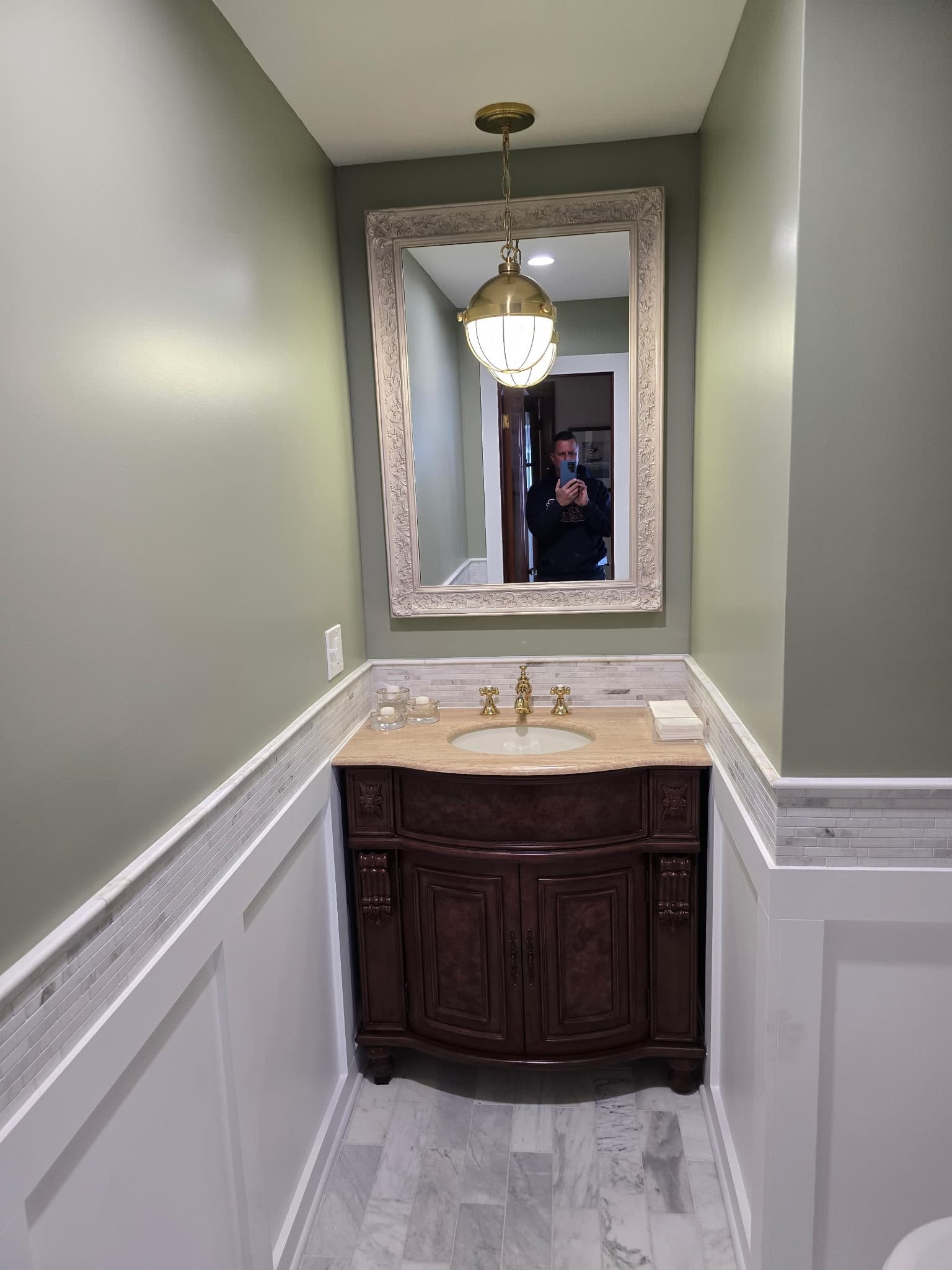 Sage green powder room with crisp paint, antique vanity, and brass pendant lighting
